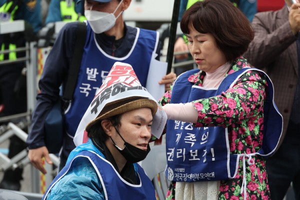 2023년 4월20일 서울 용산구 6호선 삼각지역 10번출구 인근에서 열린 ‘420발달장애인 권리보장 촉구대회’에서 한 참석자가 다른 참석자의 머리에 구호가 적힌 작은 펼침막을 둘러주고 있다. 한겨레 김혜윤 기자 unique@hani.co.kr